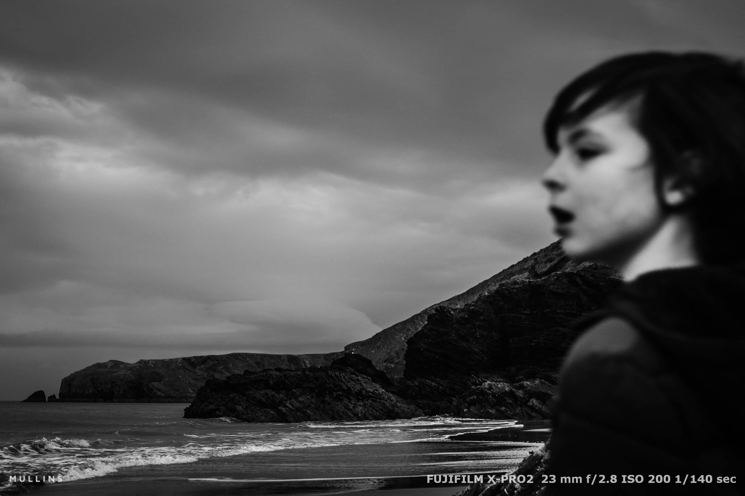 Moody seascape with a blurred child in the foreground and dramatic coastal cliffs under cloudy skies