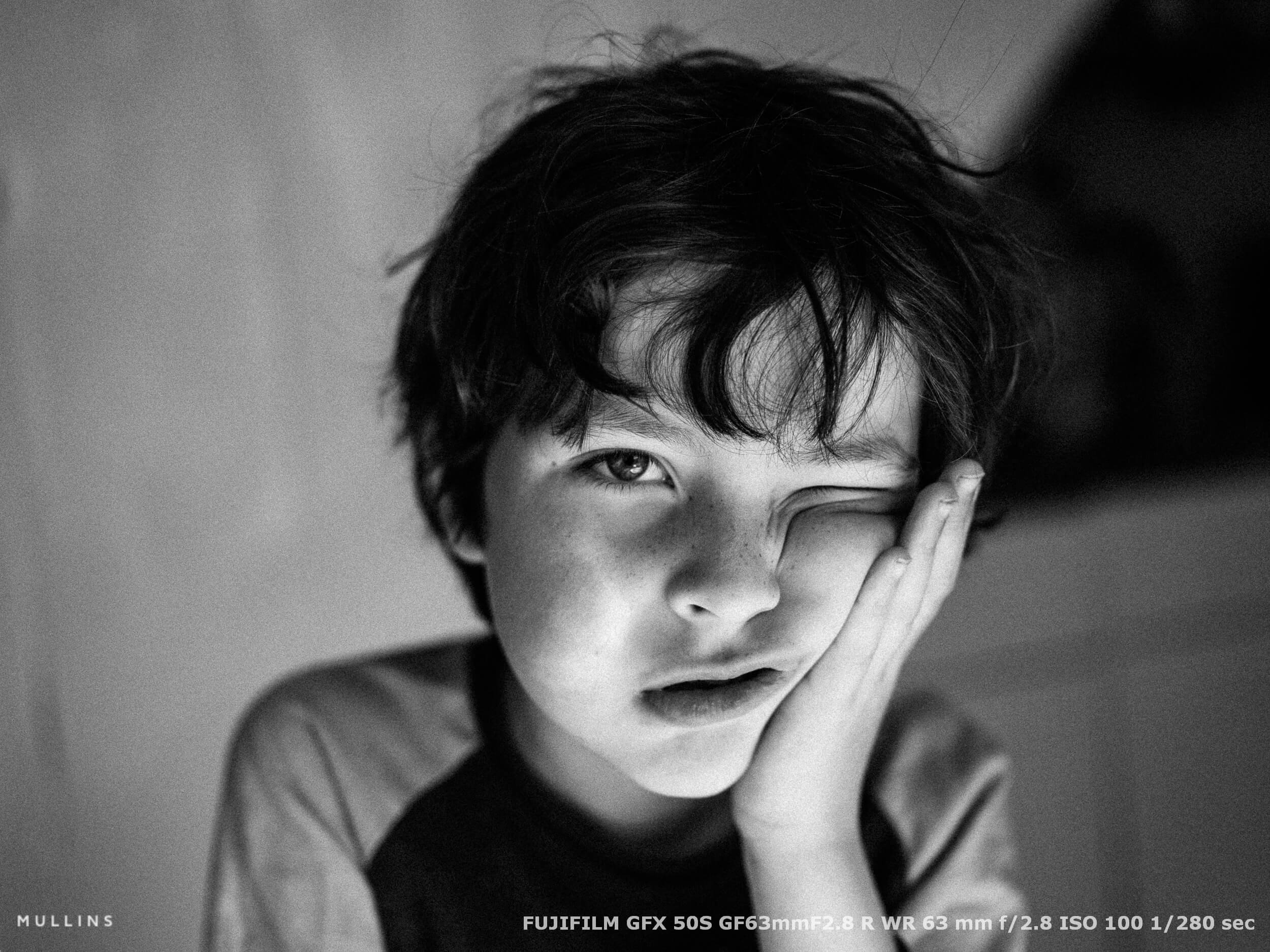 Tired child resting his face in his hand, captured in a quiet candid moment using soft window light