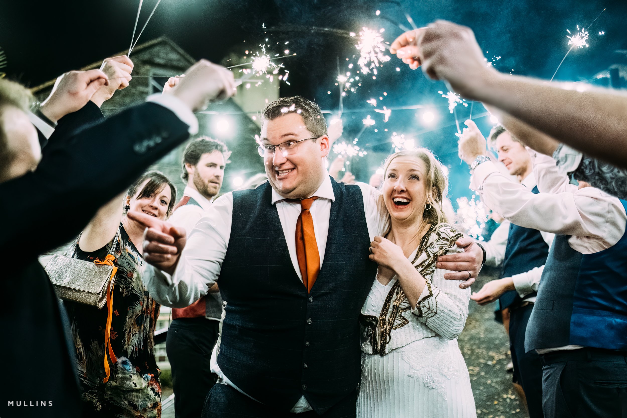 Party celebration with sparklers, people smiling, and embracing during a festive outdoor event at night.
