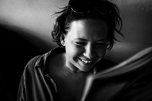 A woman smiling while looking at a book or magazine in black and white.